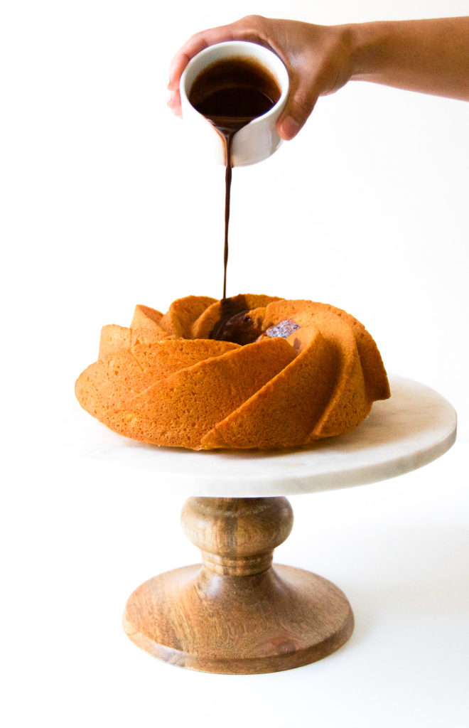 A woman drizzles chocolate sauce on top of a bundt cake