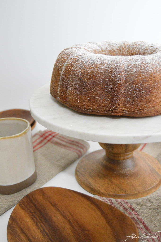 a round brown sugar spice cake on a white cake stand dusted with powdered sugar