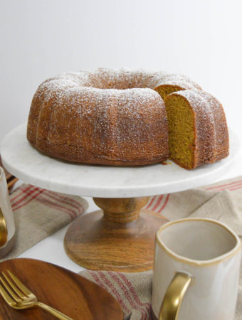 a round spice cake on a white cake stand next to a cup of coffee