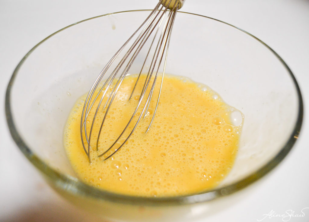 A whisk mixes an egg in a bowl