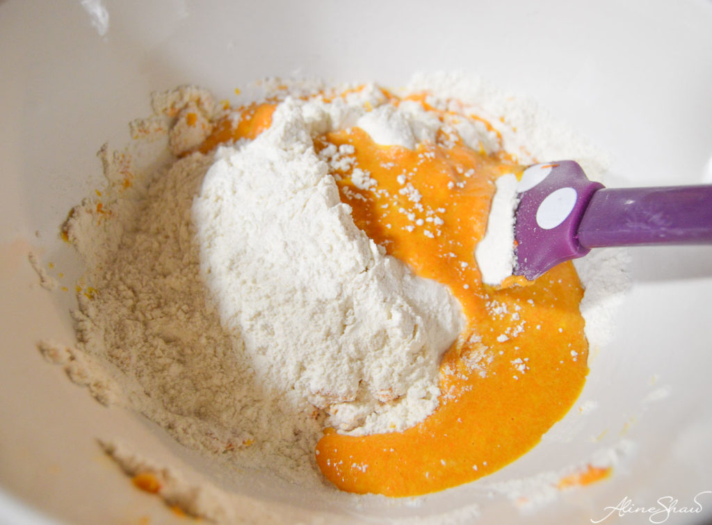 A purple spatula mixes Brazilian Carrot Cake ingredients in a white bowl