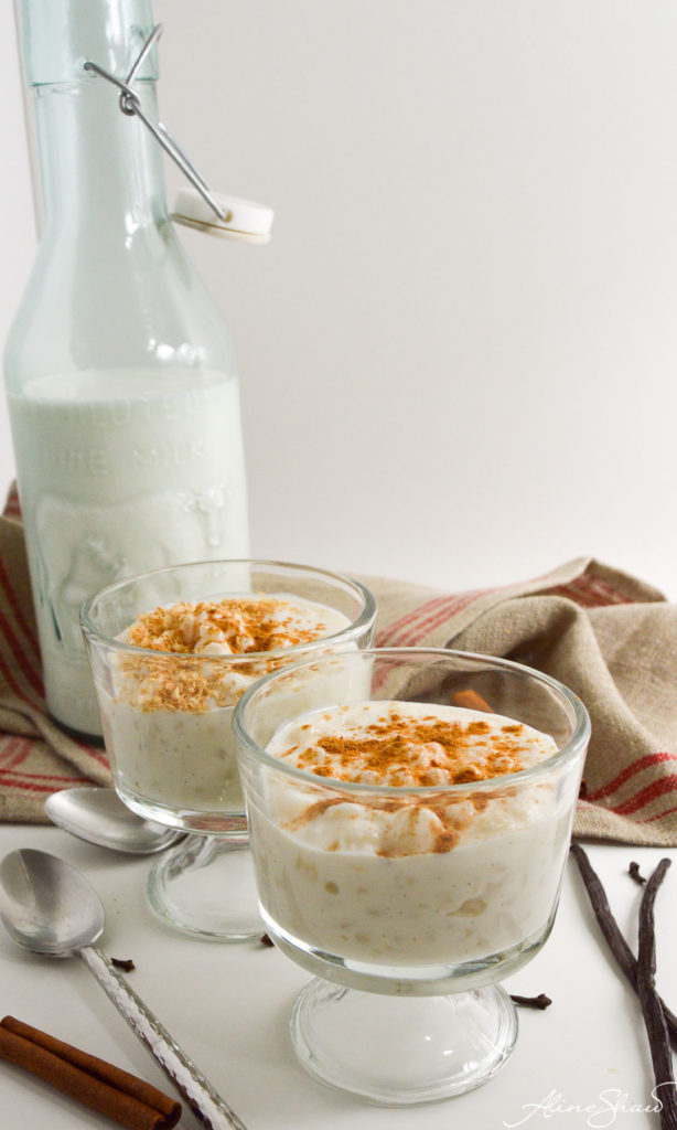 Canjica, Brazilian White Corn and Coconut Porridge, shown in two serving containers next to a bottle of milk