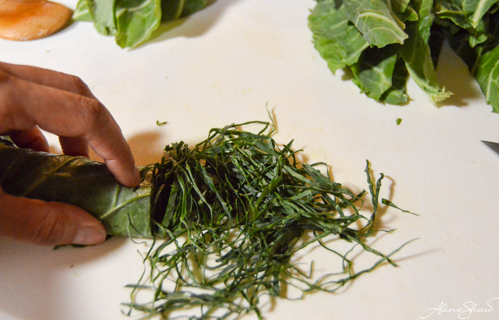 A woman holds a half cut roll of collard greens that have been chiffonaded