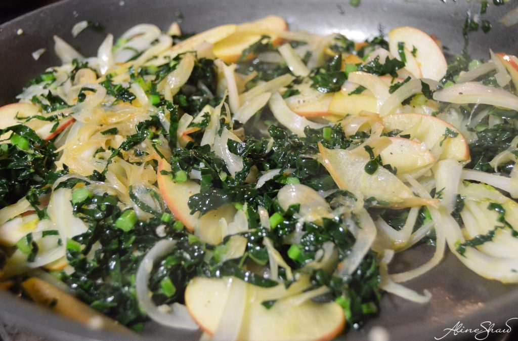 thinly sliced kale in a skillet with apples and other warm salad ingredients
