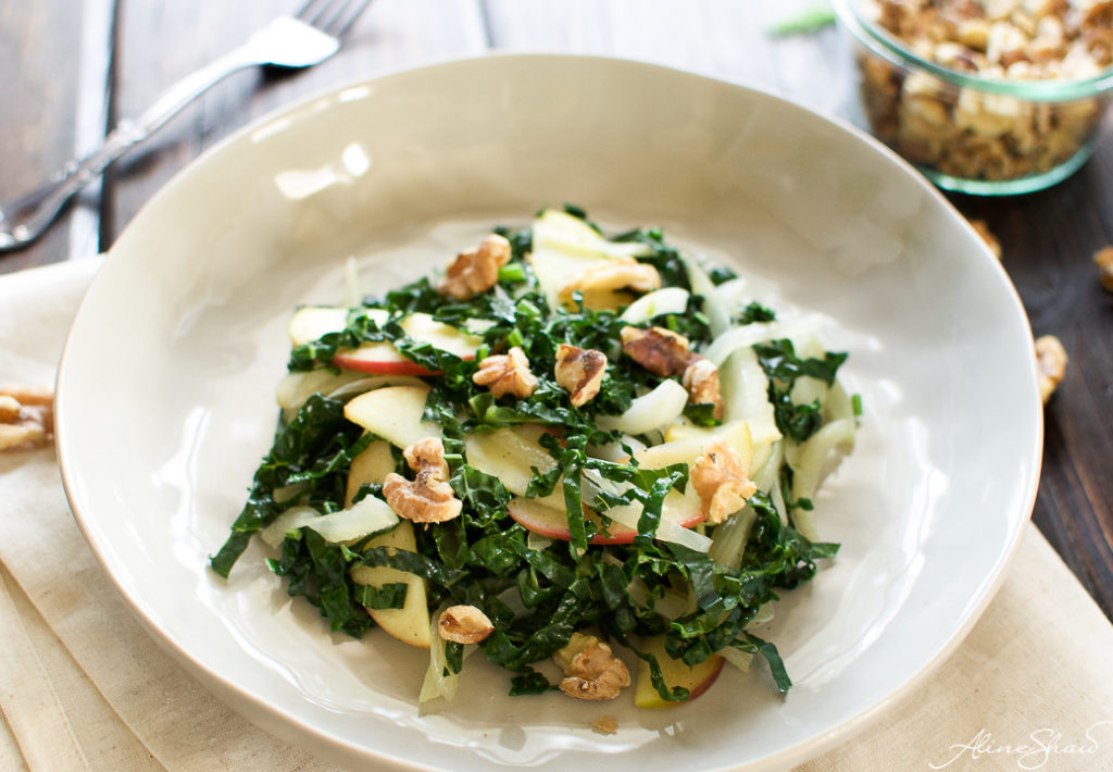 a white plate holds a serving of a warm kale salad with apples and toasted nuts