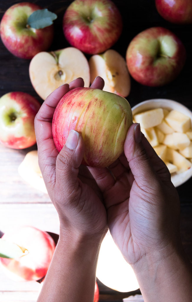 A set of hands holds sliced apples above a wooden cutting board