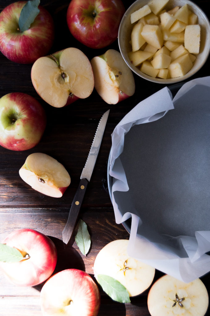 A round cake pan lined with parchment paper surrounded by sliced apples