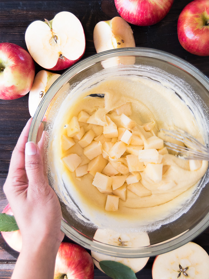 A person stirs chunks of apples into cake batter in a bowl