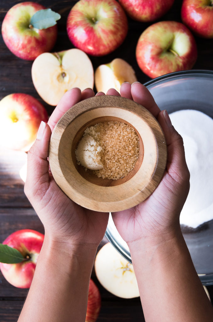 A set of hands holds a bowl of spices above chopped apples