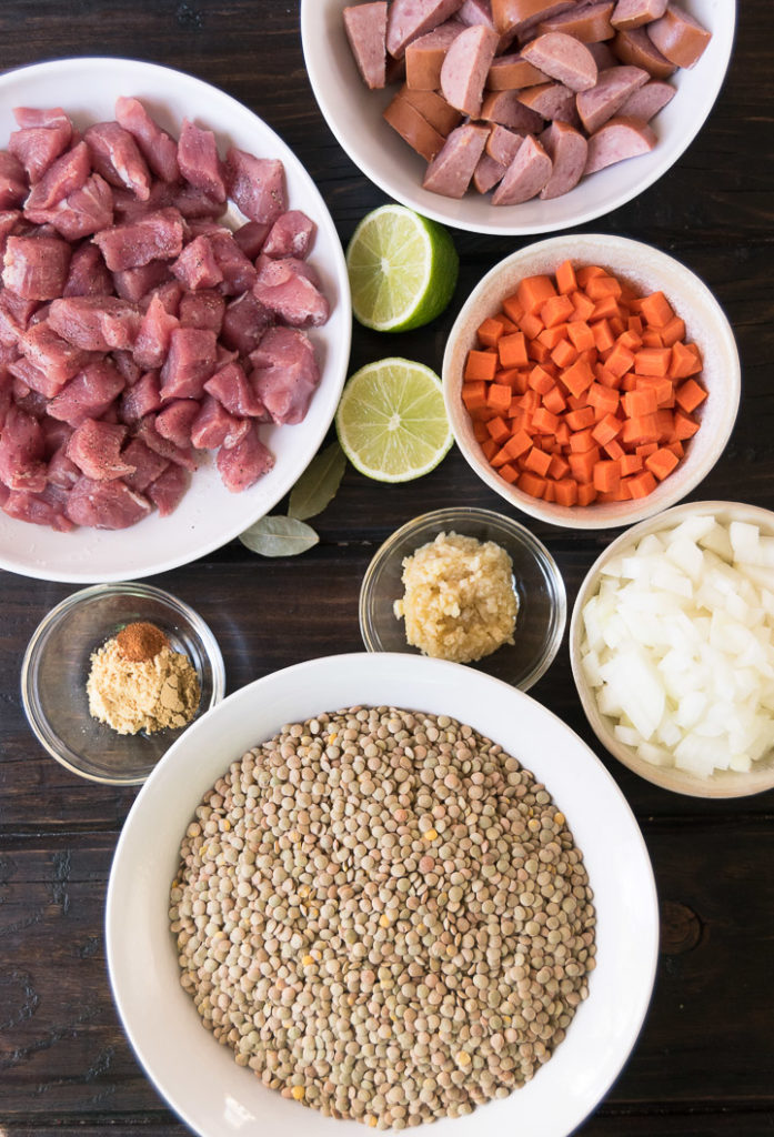ingredients to make pork lentil stew in bowls on a wooden surface