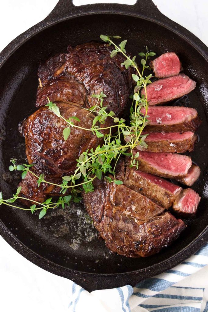 Two ribeye steaks in a skillet with fresh thyme over them
