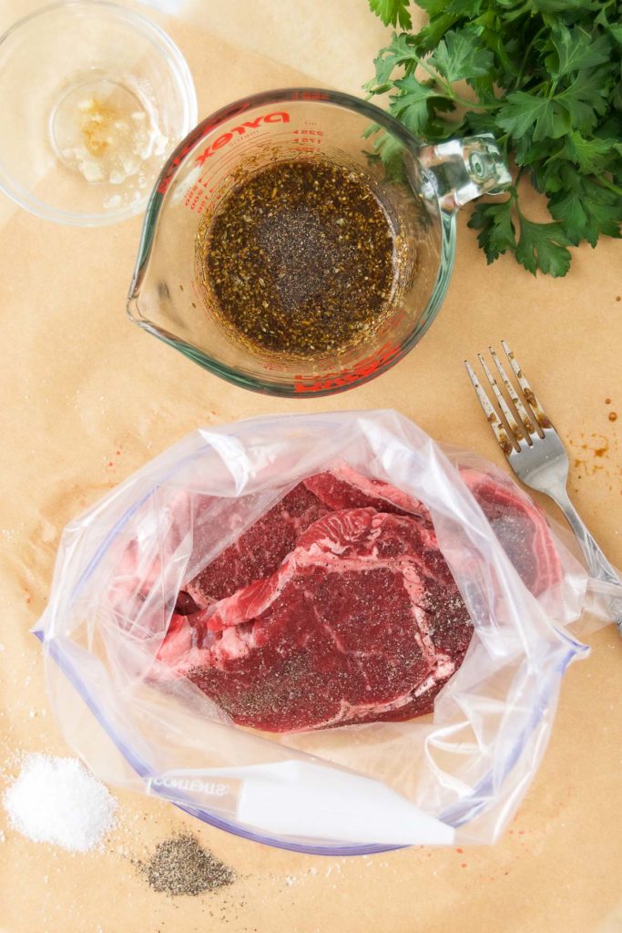 Steaks in a gallon-sized plastic bag next to marinade