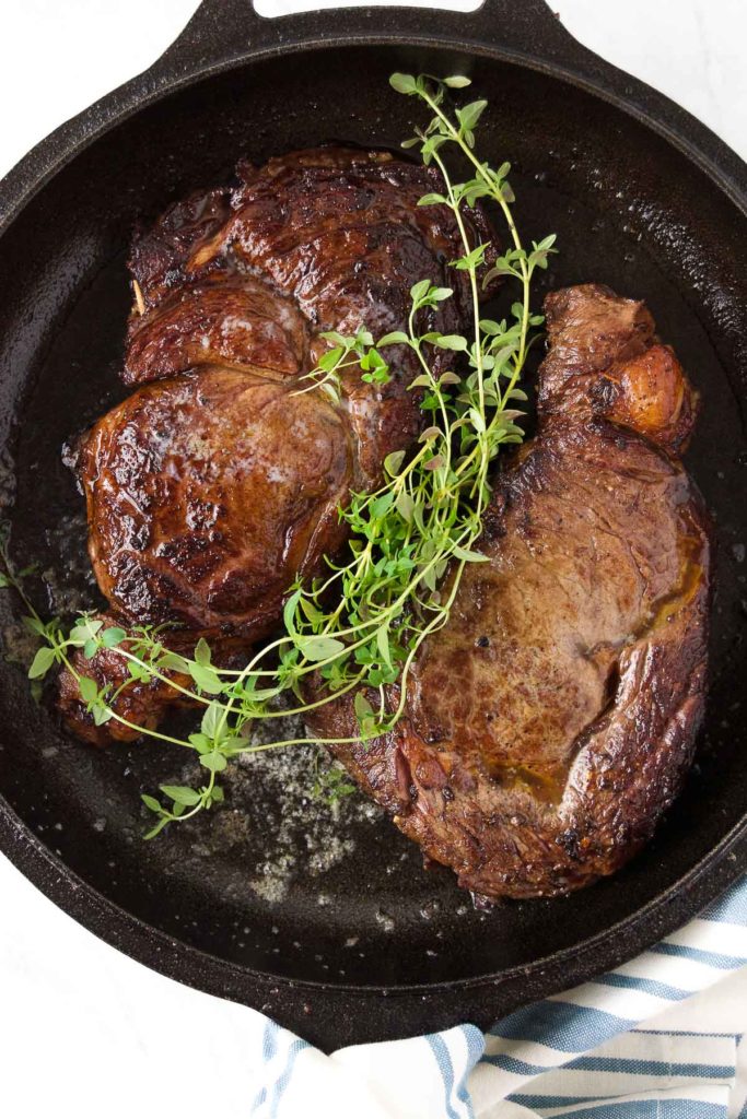 Two ribeye steaks in a skillet topped with fresh thyme