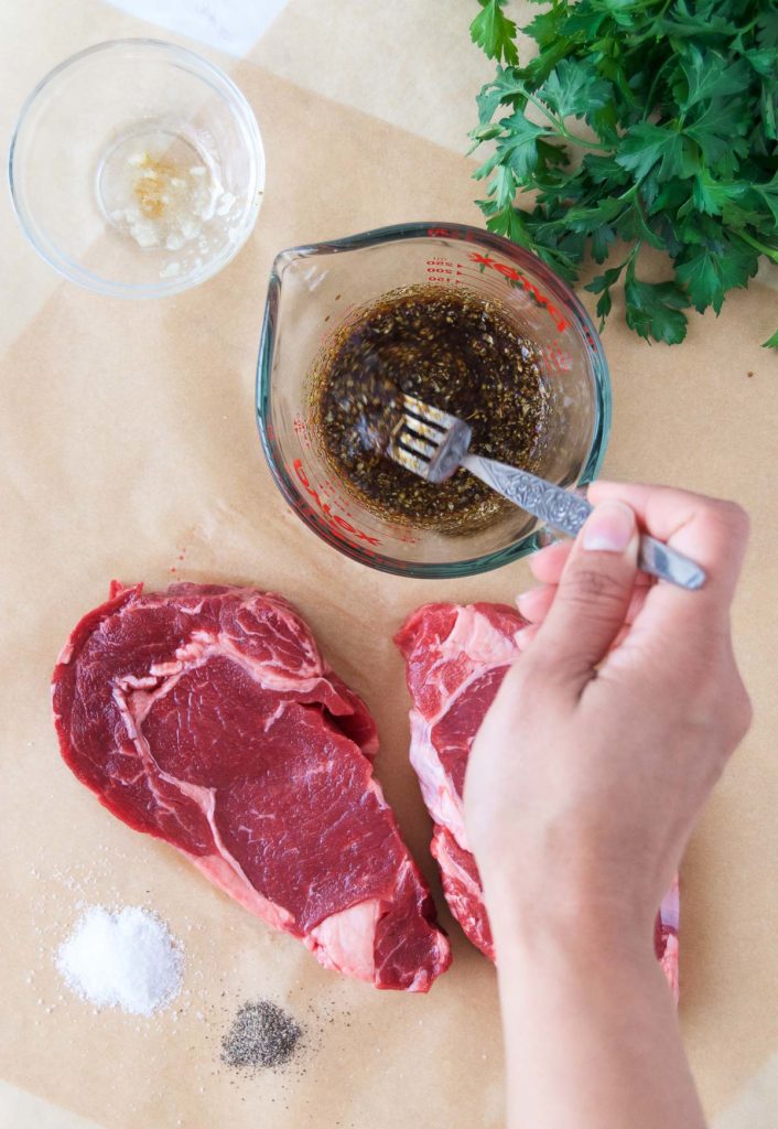 A woman stirs a steak marinade with a fork next to steaks