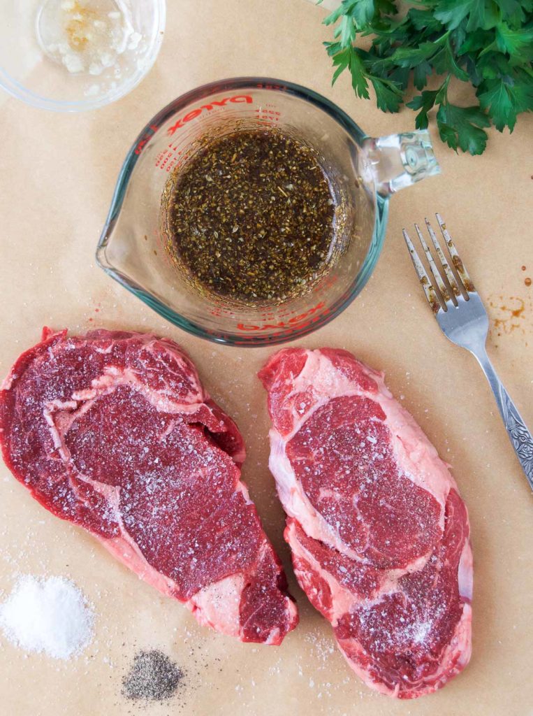 Two ribeye steaks sit next to a bowl of marinade