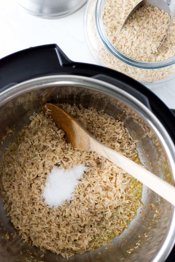 brown rice and salt sit in the instant pot with a wooden spoon