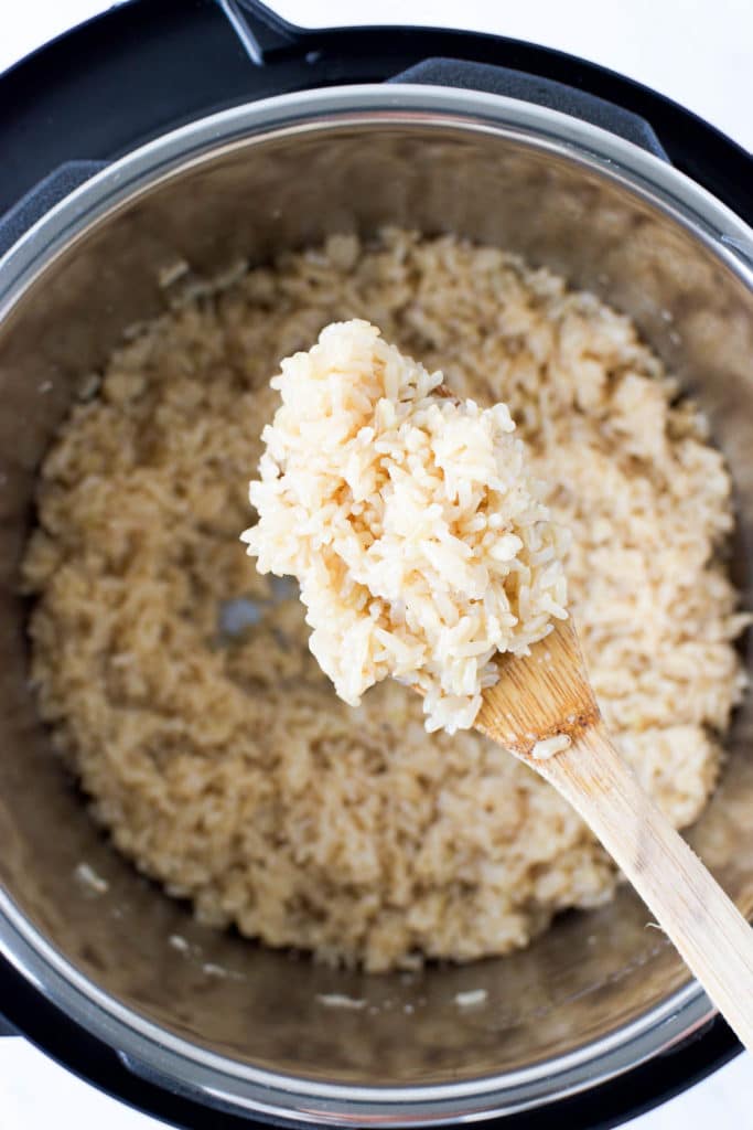 a wooden spoon lifts brown rice out of the electric pressure cooker