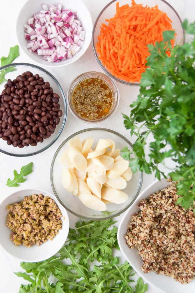 ingredients to make a vegan quinoa salad in bowls on a marble surface
