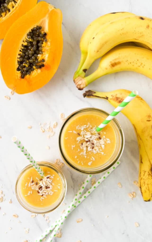 two tropical smoothies surrounded by banana and papaya from above