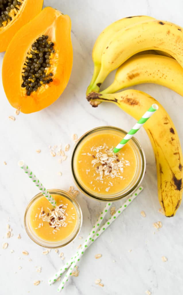 two banana papaya smoothies from above on marble, surrounded by ingredients