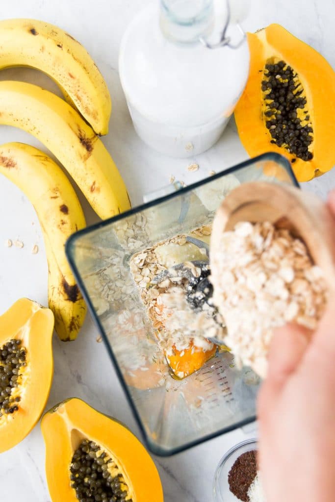 oats are poured into a blender, surrounded by banana and papaya