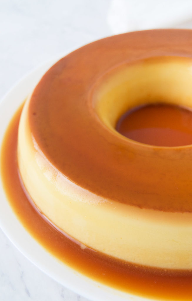 Close up of a Brazilian Flan on a white platter with its caramel sauce everywhere