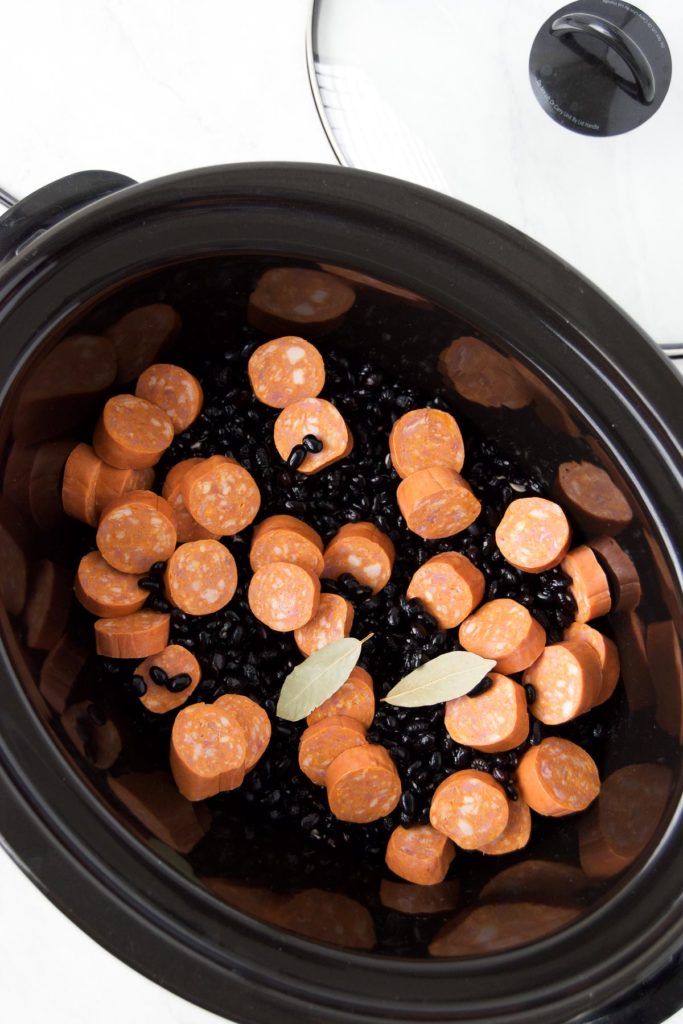 Black beans, sausage and bay leaf in a slow cooker basin