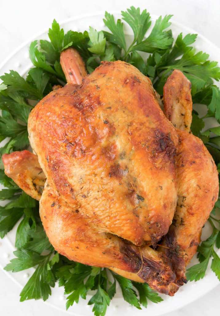 A whole roasted chicken sits on a bed of greens 