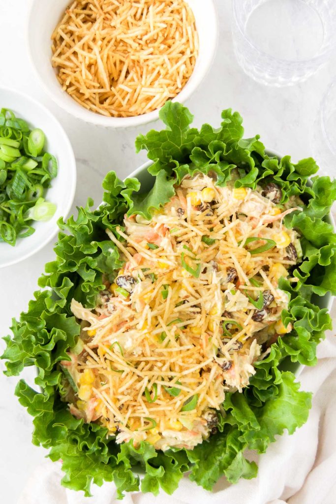 Brazilian chicken salad in a serving dish, surrounded by salad greens