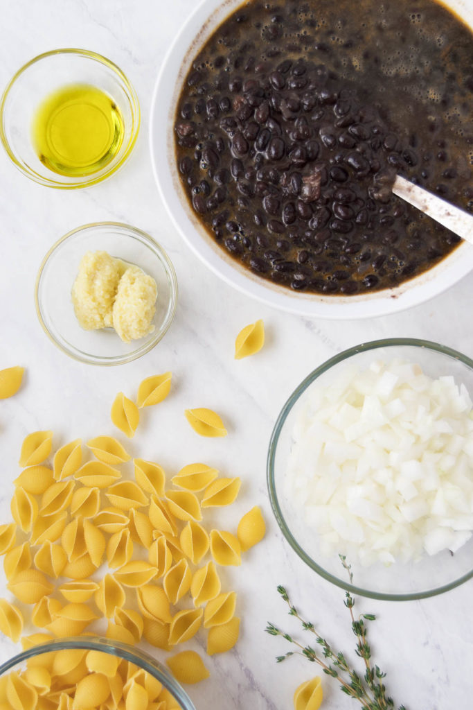 Bowls of beans and onions next to pasta on a marble surface