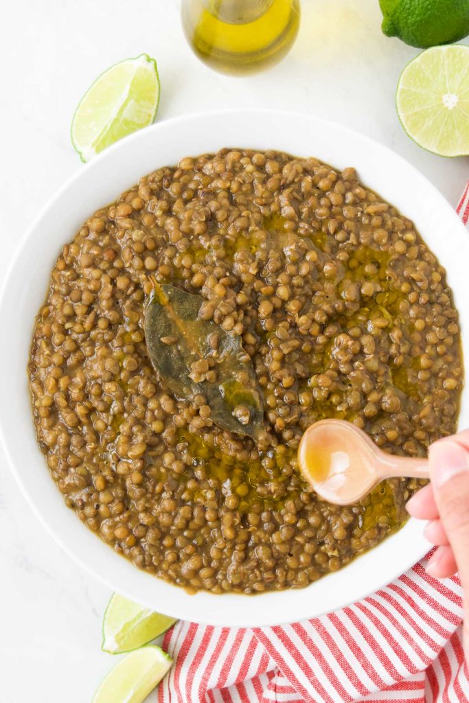 Olive oil drizzles over cooked green lentils in a bowl
