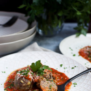A fork holds a sliced meatball in tomato sauce on a plate