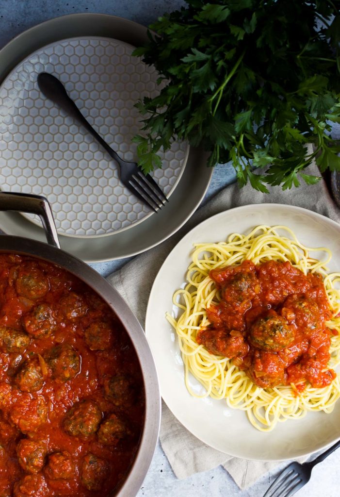 A plate of pasta and meatballs next to a skillet of sauce