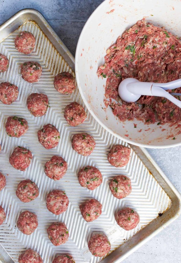 Sausage meatballs scooped onto a baking sheet next to a bowl and scooper