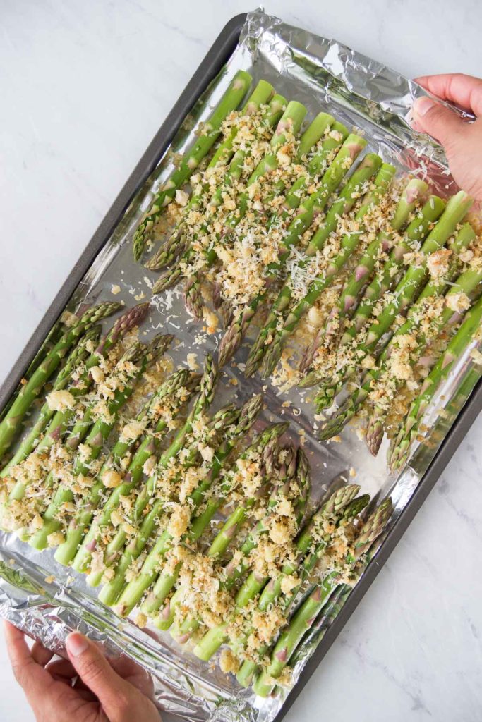 A woman holds a sheet pan of Baked Asparagus with Parmesan