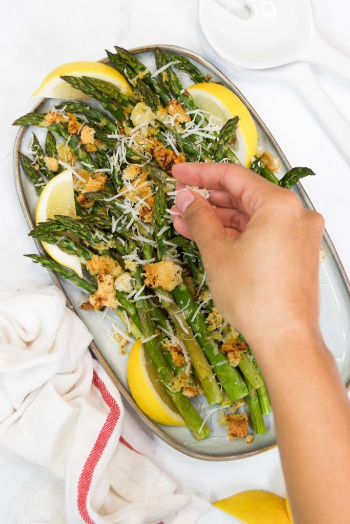 A woman sprinkles cheese on top of Baked Asparagus with Parmesan