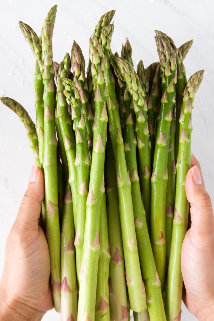 A woman holds a bunch of green asparagus between her hands