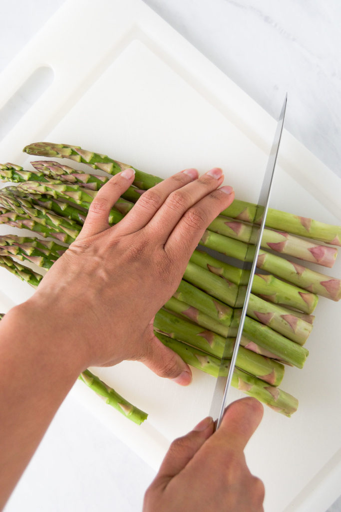 A woman cuts a bunch of asparagus on a cutting board