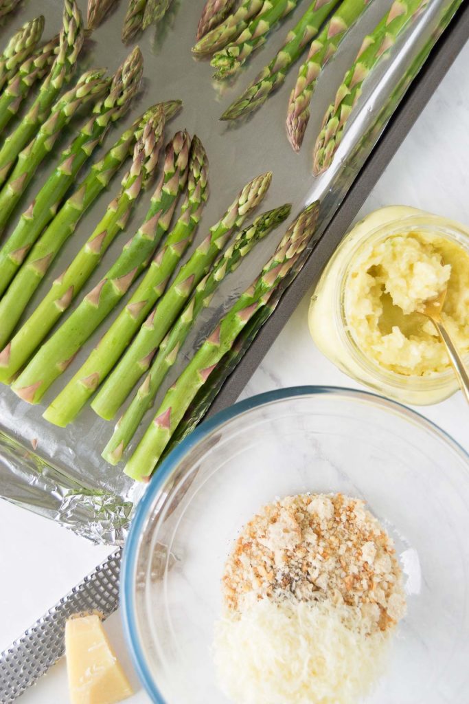 Asparagus on a baking sheet with parmesan and bread crumb seasoning in a bowl