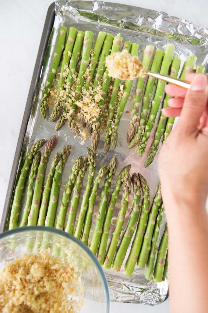 A parmesan topping sprinkles onto a sheet pan of asparagus