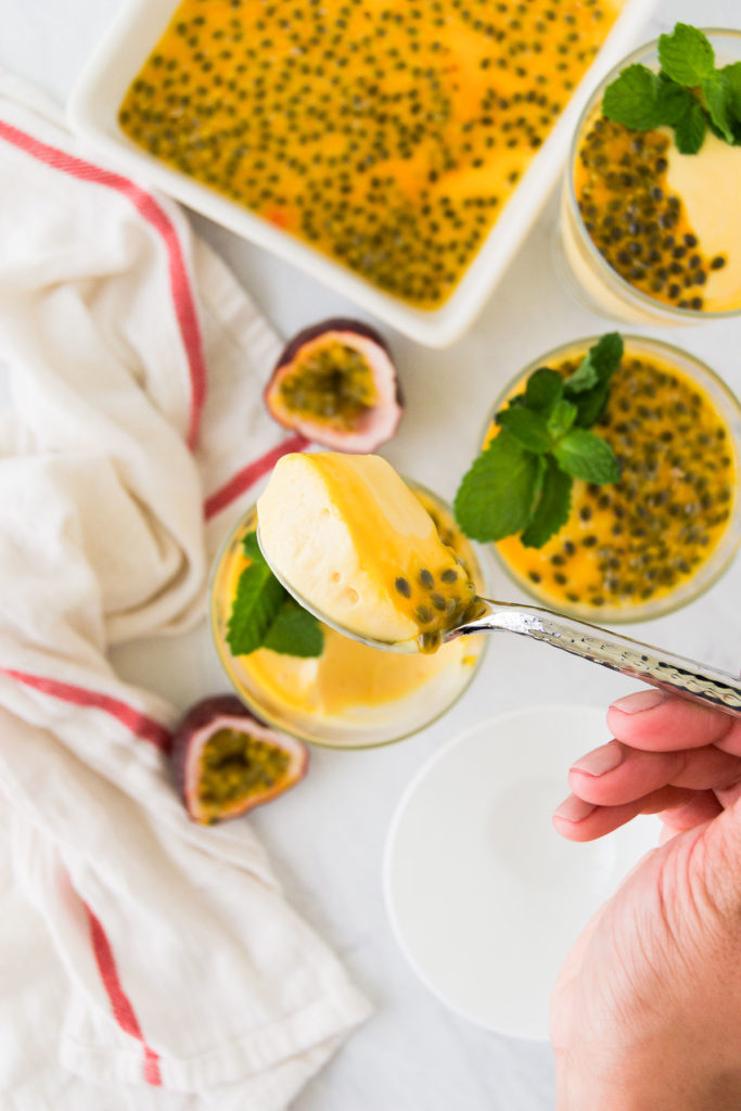 A spoon holds a scoop of a thick passion fruit dessert with passion fruit seeds on top