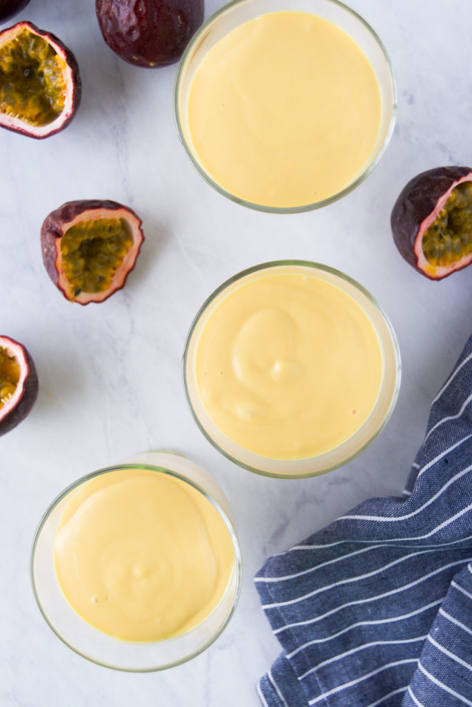 Three small bowls of mousse sit near passion fruit before chilling