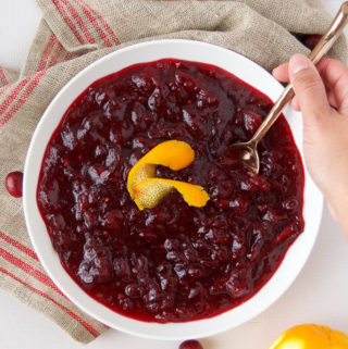 A person spoons a scoop of Cranberry Sauce from a big bowl