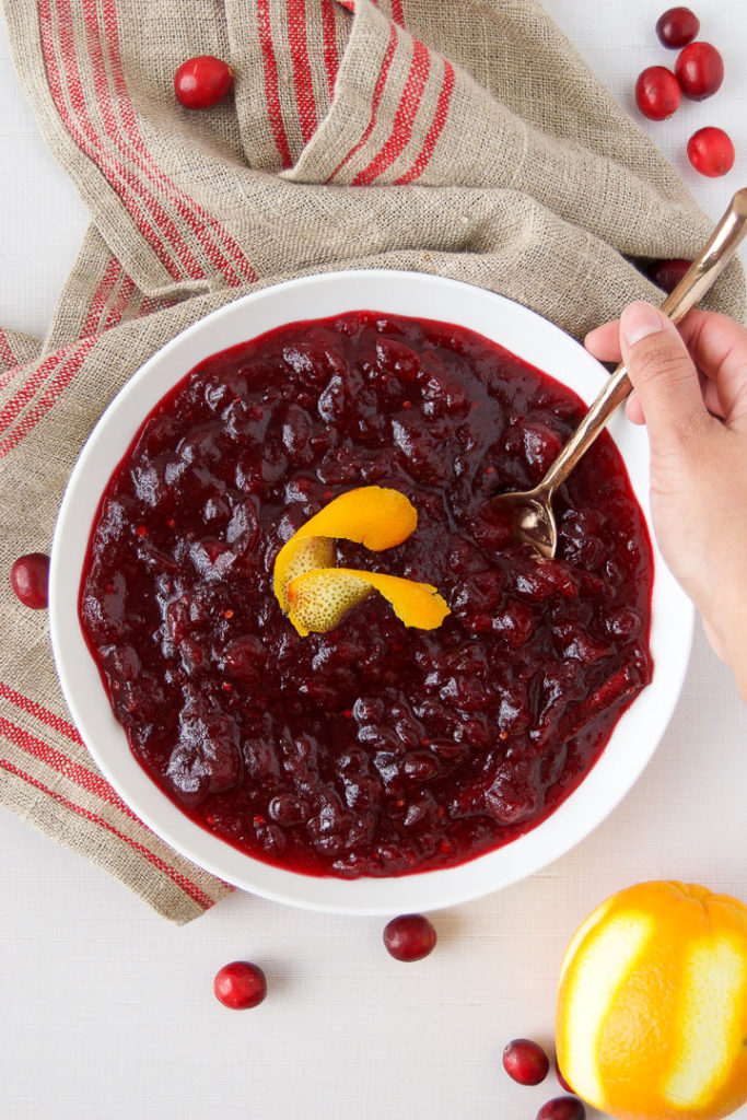 A person spoons a scoop of Cranberry Sauce from a big bowl