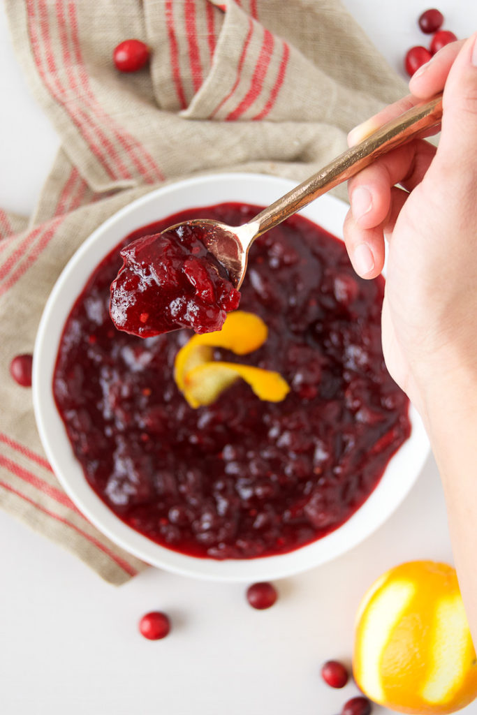 A person lifts a spoonful of homemade cranberry sauce from a bowl on a table