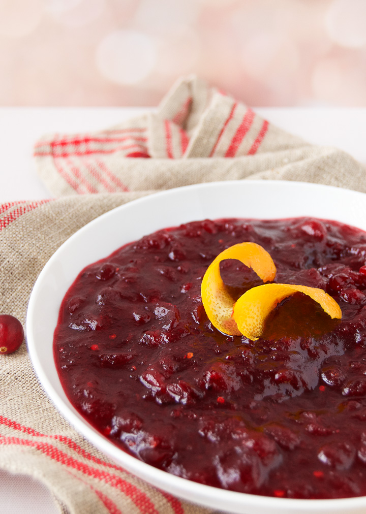 An orange curl sits on top of a bowl of fresh cranberry sauce