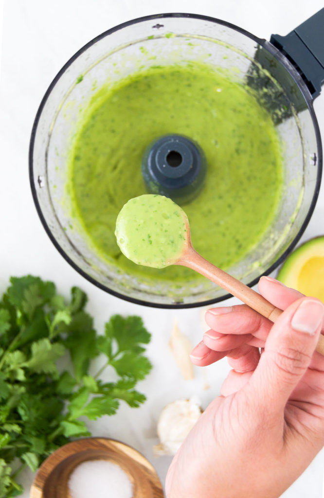 A person holds a spoon of Lime Avocado Dressing above a food processor