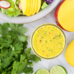 A mason jar of bright yellow mango dressing next to salad ingredients
