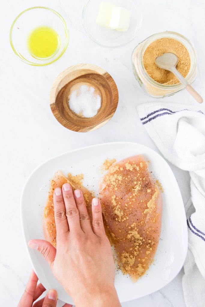 A hand massages seasoning into a chicken breast