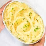 A woman holds a bowl of Instant Pot Mashed Potatoes garnished with butter and chives